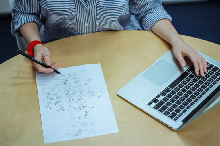 a person sitting at a table with a laptop and a piece of paper